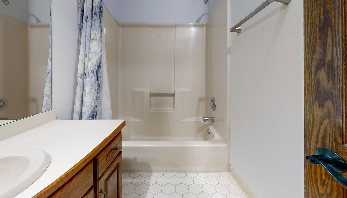 Sol de salle de bain en carreaux hexagonaux clairs, baignoire et meuble bois en arrière-plan Image